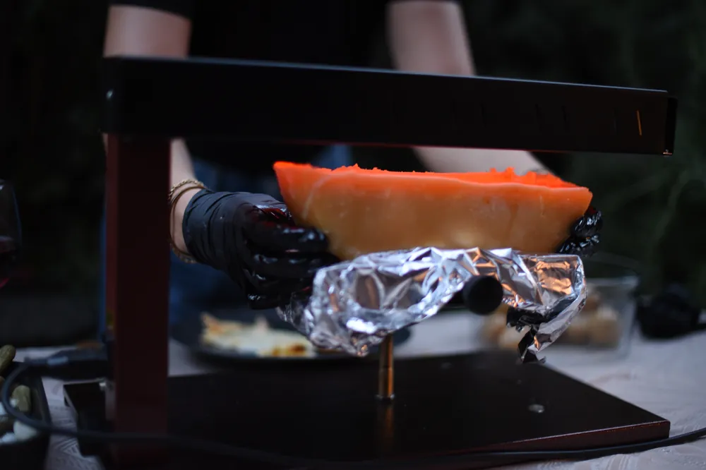 Raclage d'une demi-meule de fromage à raclette valaisan fondu