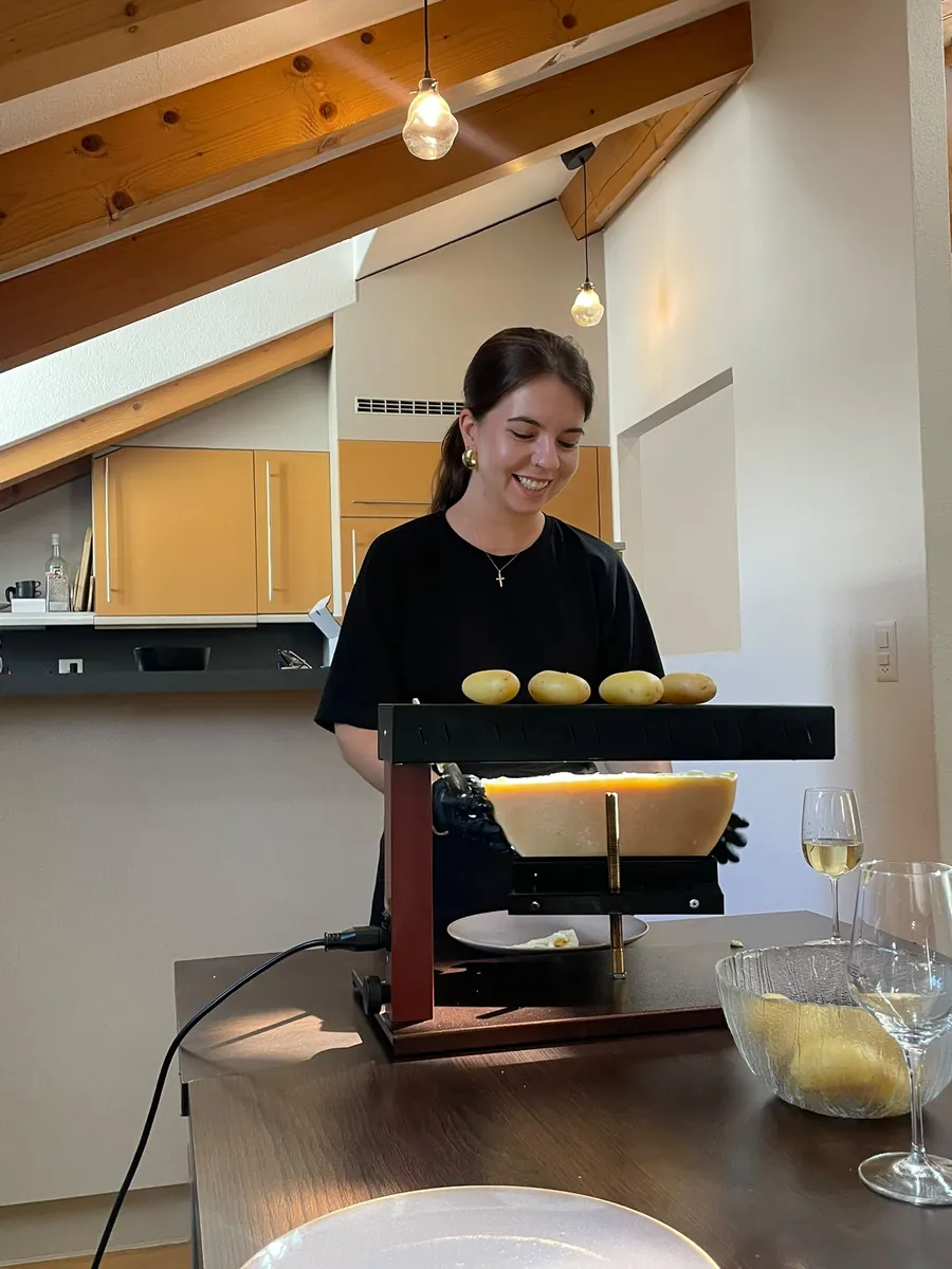Racleuse raclant une demi-meule de fromage valaisan lors d'une raclette à domicile dans un chalet